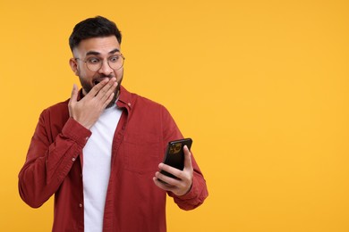 Photo of Emotional young man using smartphone on yellow background, space for text