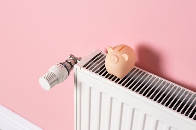 Photo of Heating radiator with piggy bank on color wall