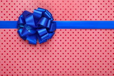 Photo of Blue ribbon with bow on red polka dot wrapping paper, top view. Space for text