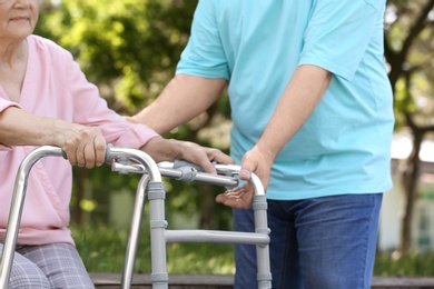Photo of Elderly man helping his wife with walking frame outdoors, closeup