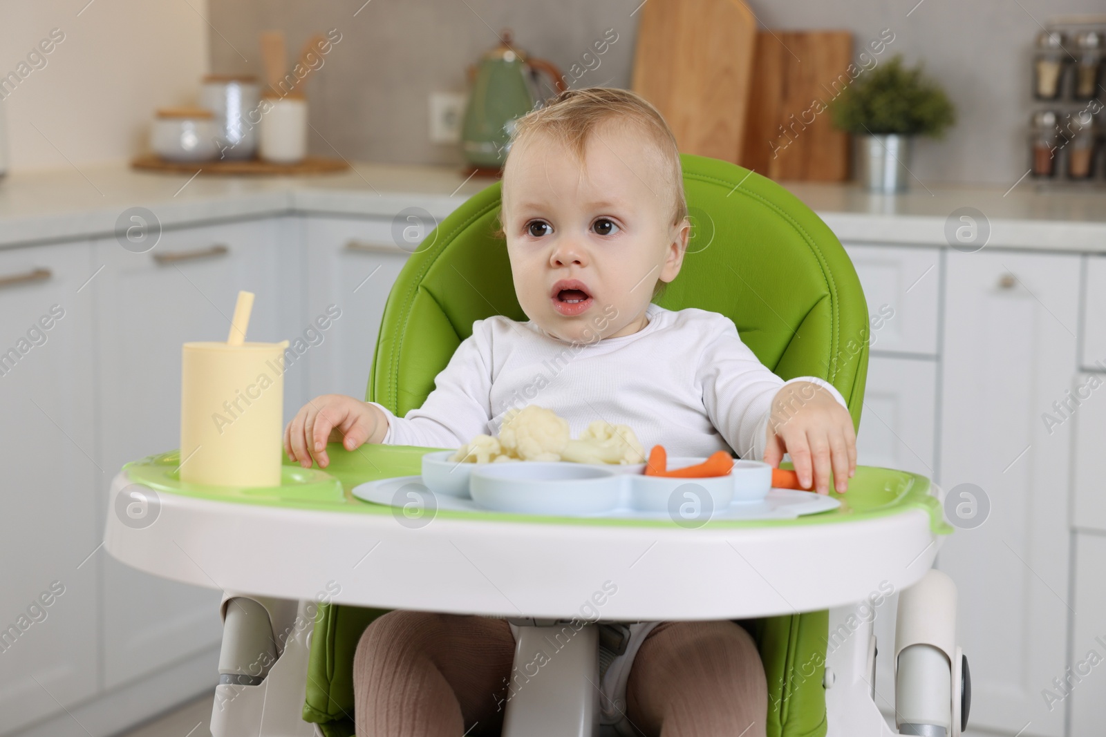 Photo of Cute little baby with healthy food in high chair at home