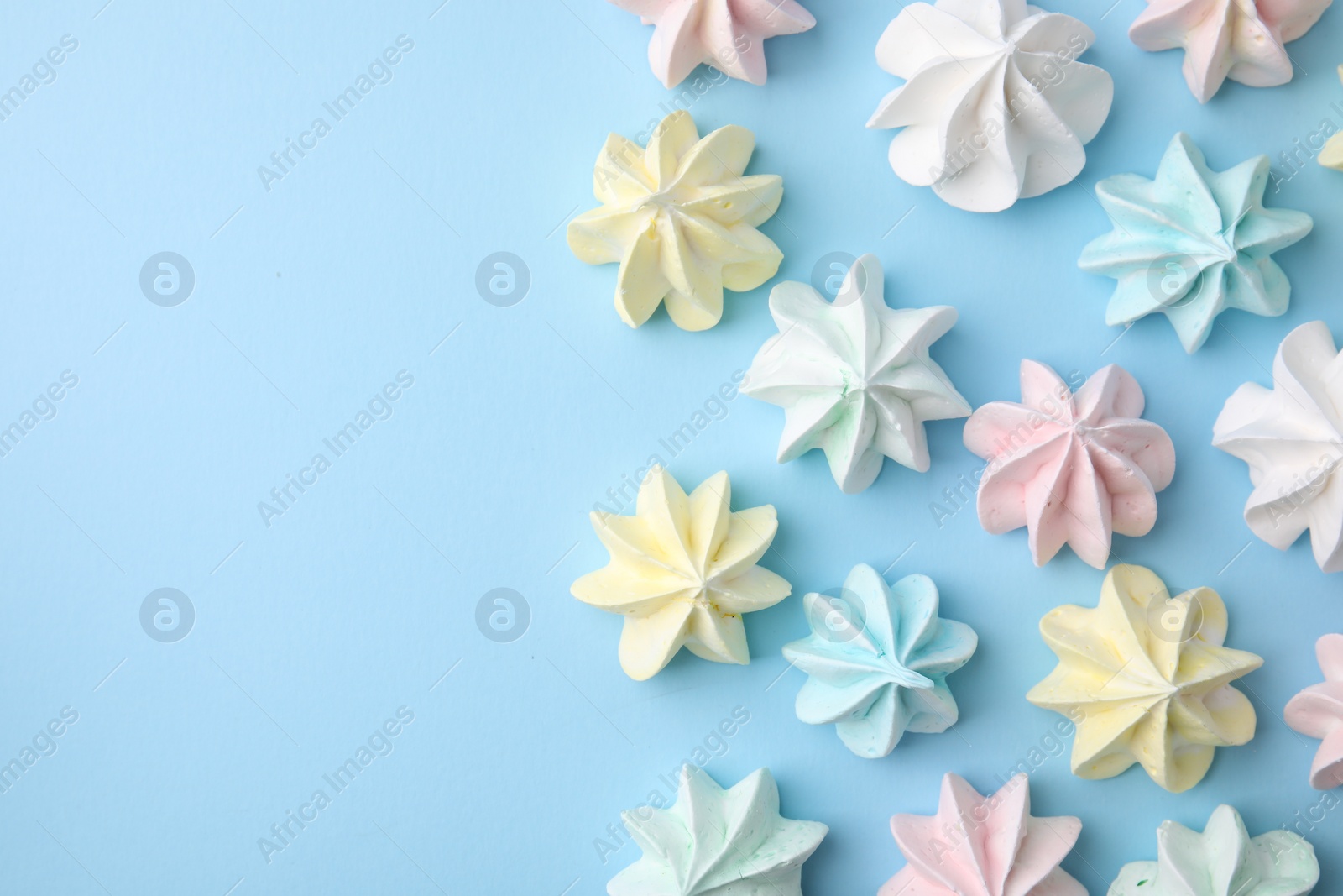 Photo of Tasty meringue cookies on light blue background, flat lay. Space for text