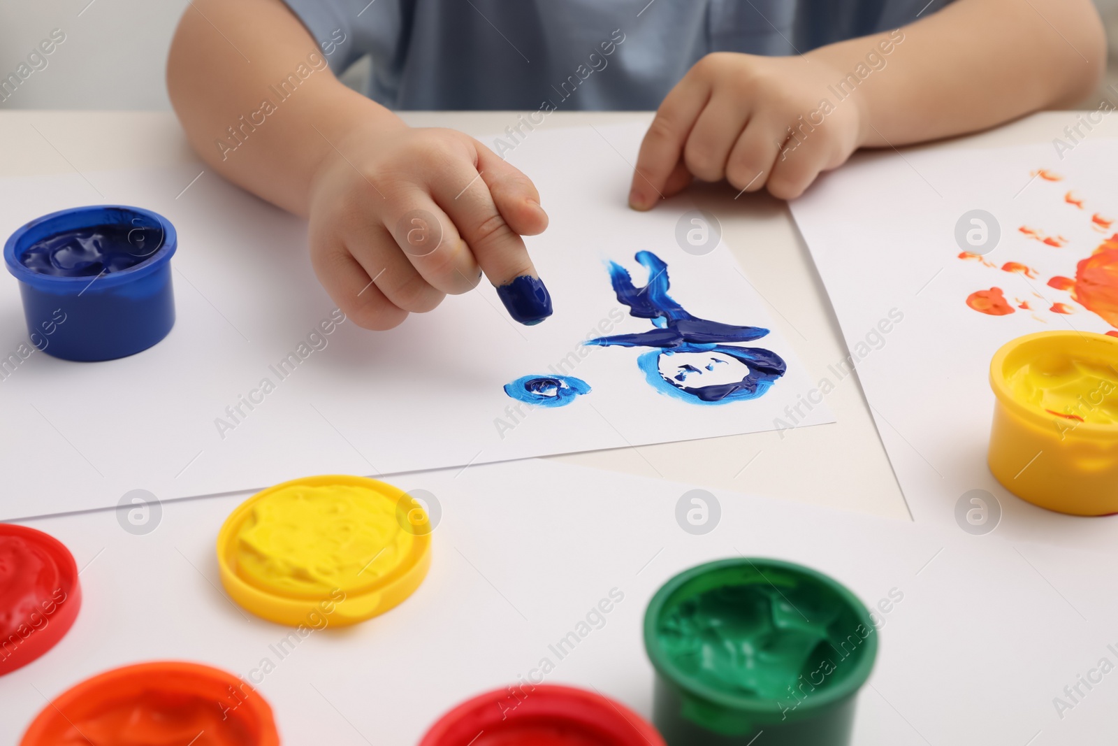 Photo of Little child painting with finger at white table indoors, closeup