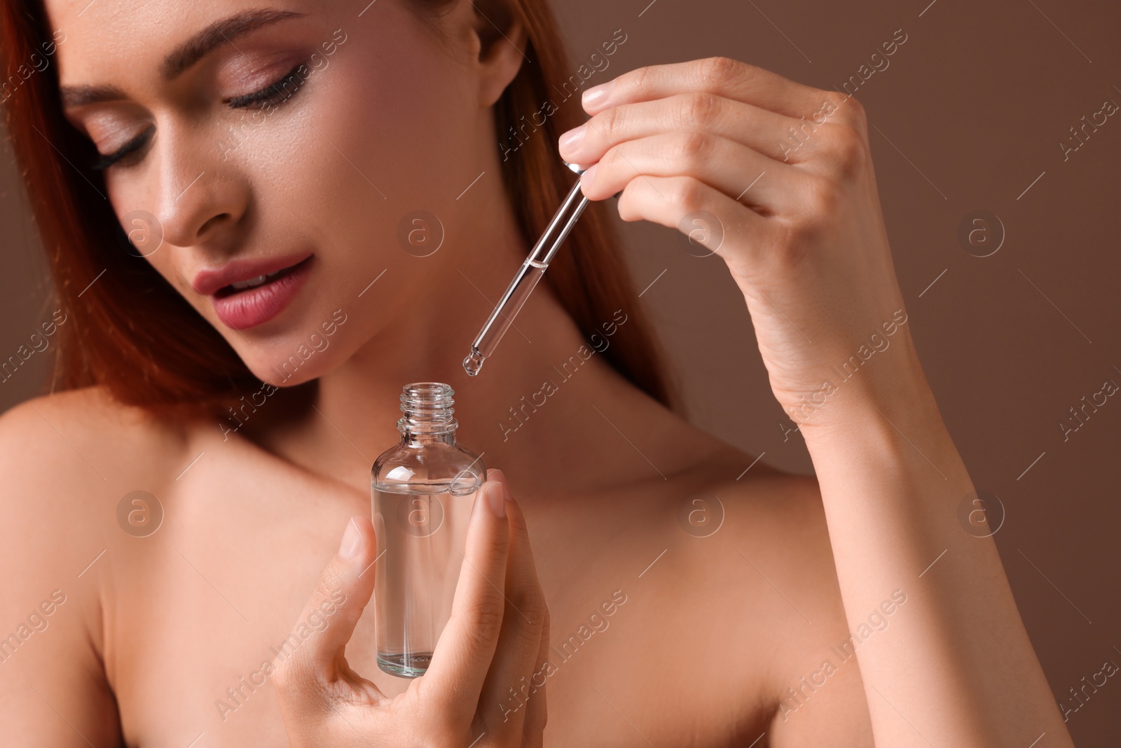 Photo of Beautiful young woman with bottle of cosmetic serum on brown background, closeup