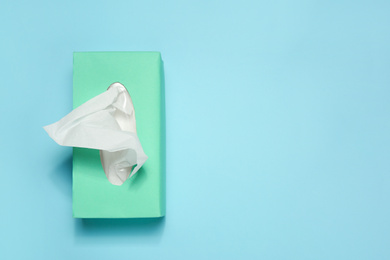 Photo of Box with paper tissues on light blue background, top view. Space for text