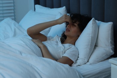 Photo of Young woman suffering from headache in bed at night