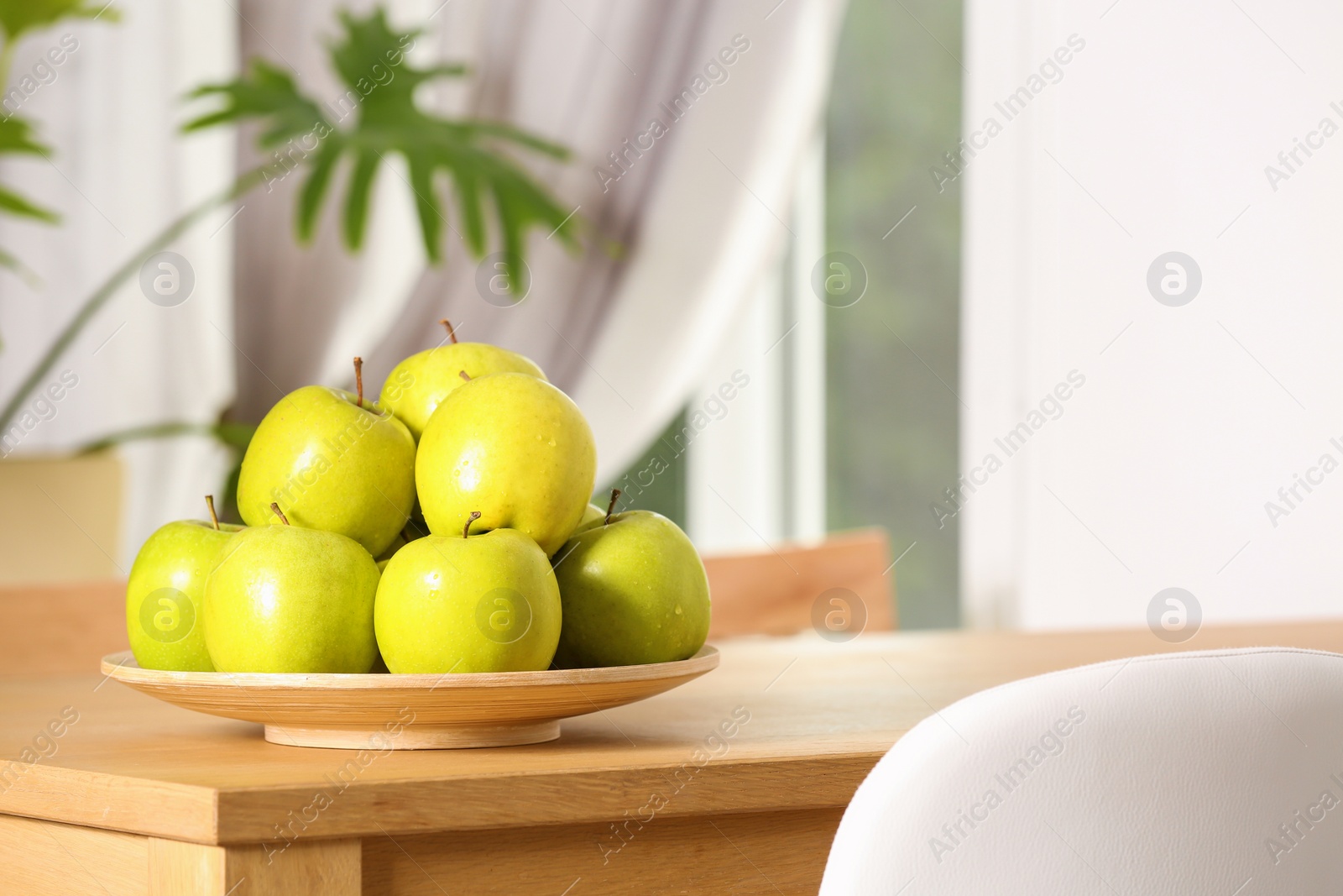 Photo of Plate with sweet green apples on table in room, space for text