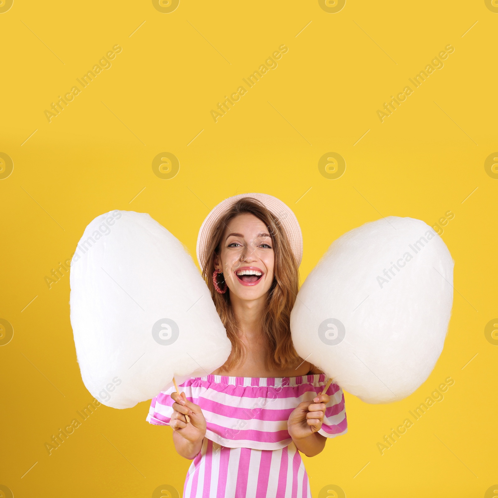 Photo of Happy young woman with cotton candies on yellow background