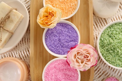 Photo of Bowls with sea salt, soap bars, jar of cream and roses on wicker mat, flat lay