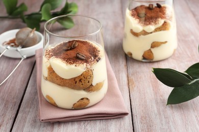 Delicious tiramisu with coffee beans in glasses and green leaves on wooden table