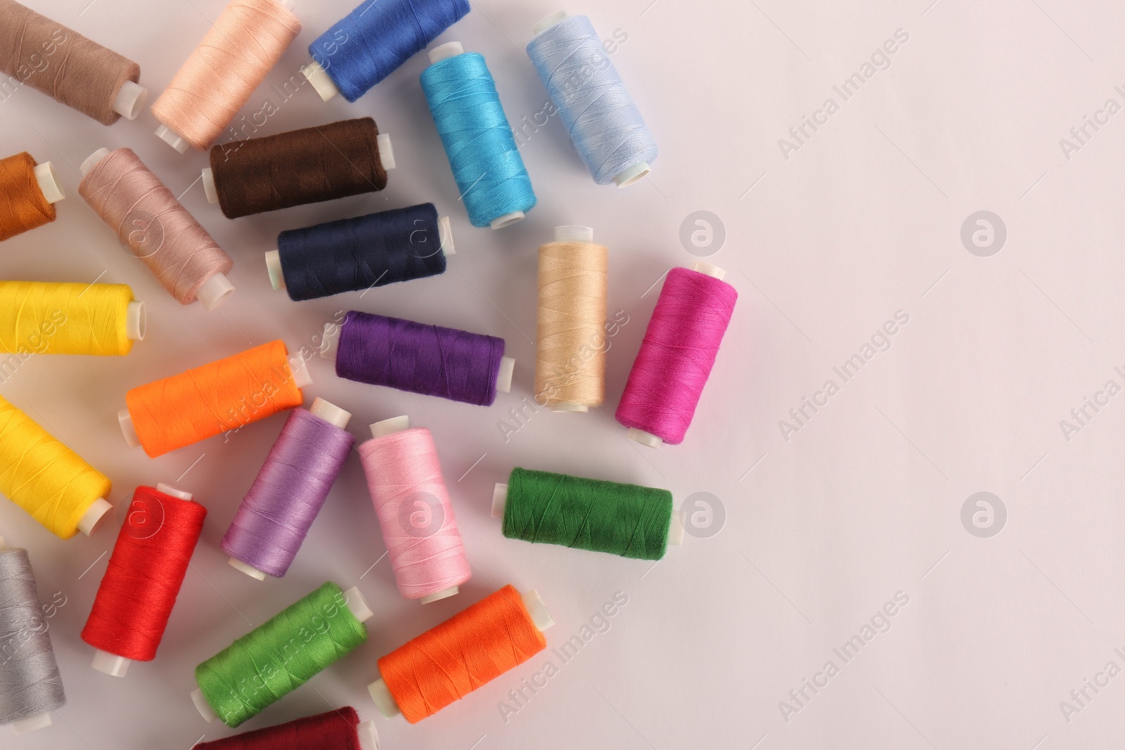 Photo of Set of colorful sewing threads on white background, top view