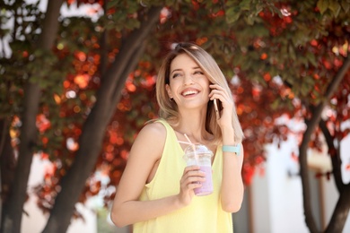 Young woman with plastic cup of healthy smoothie outdoors