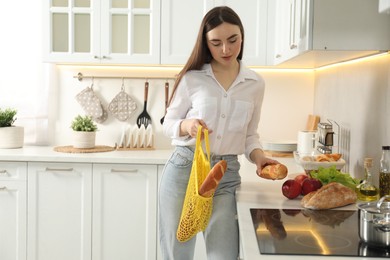 Woman holding string bag with baguettes in kitchen