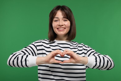 Photo of Happy woman showing heart gesture with hands on green background