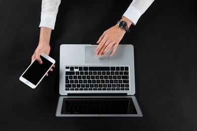 Young woman with mobile phone using laptop on black background, top view