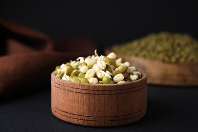 Photo of Wooden bowl with sprouted green mung beans on black background, closeup