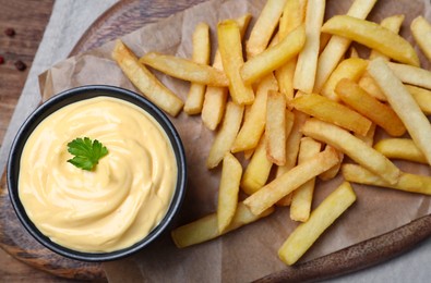 Photo of Delicious French fries and cheese sauce with parsley on wooden table, top view