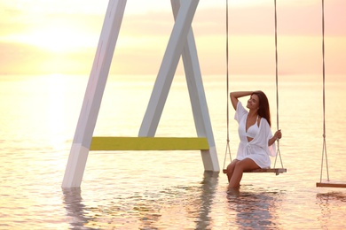 Photo of Young woman enjoying sunrise on swing over water