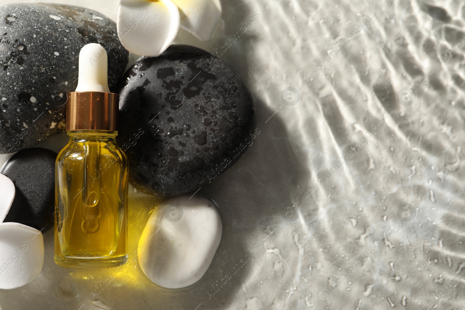 Photo of Bottle of face serum and spa stones in water on light background, flat lay. Space for text