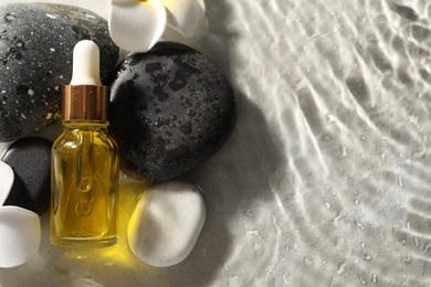 Bottle of face serum and spa stones in water on light background, flat lay. Space for text