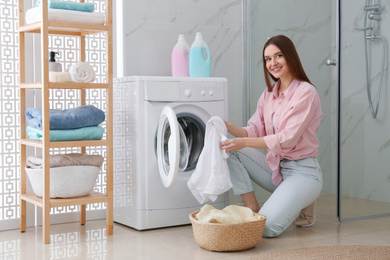 Young woman with clothes near washing machine in bathroom. Laundry day
