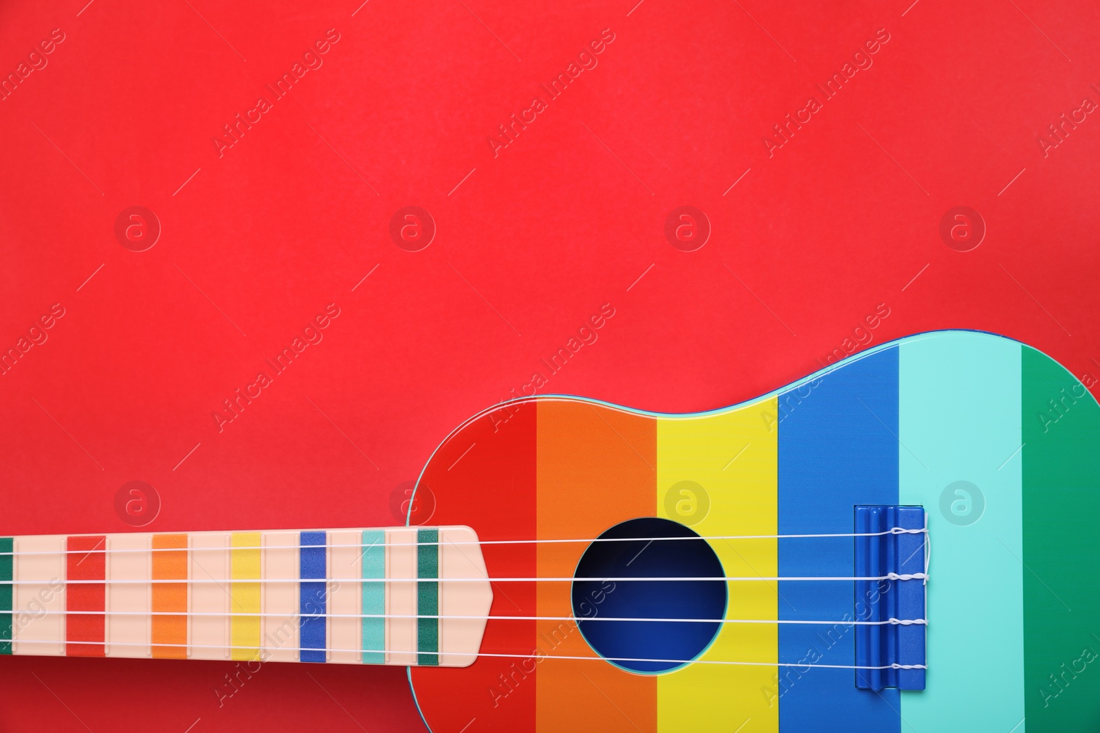 Photo of Colorful ukulele on red background, top view. String musical instrument