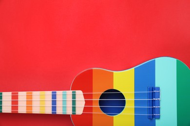 Photo of Colorful ukulele on red background, top view. String musical instrument