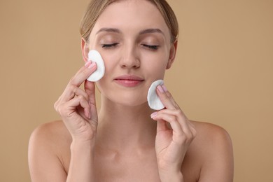 Photo of Young woman cleaning her with cotton pads on beige background