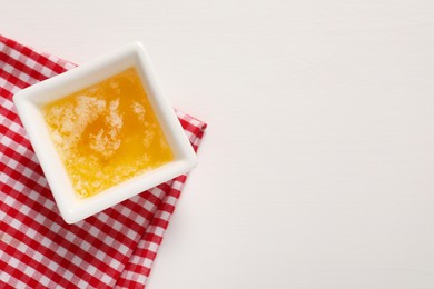 Photo of Melted butter in bowl on white wooden table, top view. Space for text