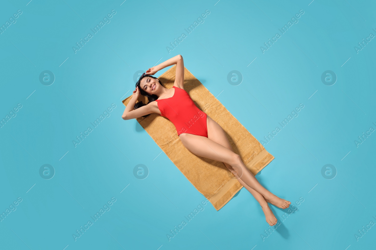 Photo of Young woman in stylish swimsuit on beach towel against light blue background
