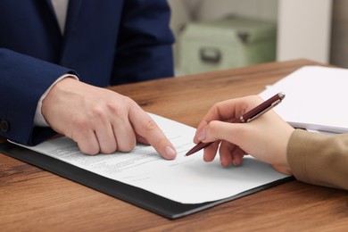 Photo of Man pointing at document and woman putting signature at wooden table, closeup