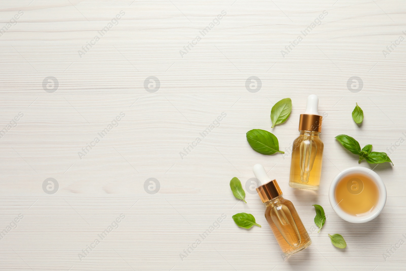 Photo of Essential basil oil and fresh leaves on white wooden table, flat lay. Space for text