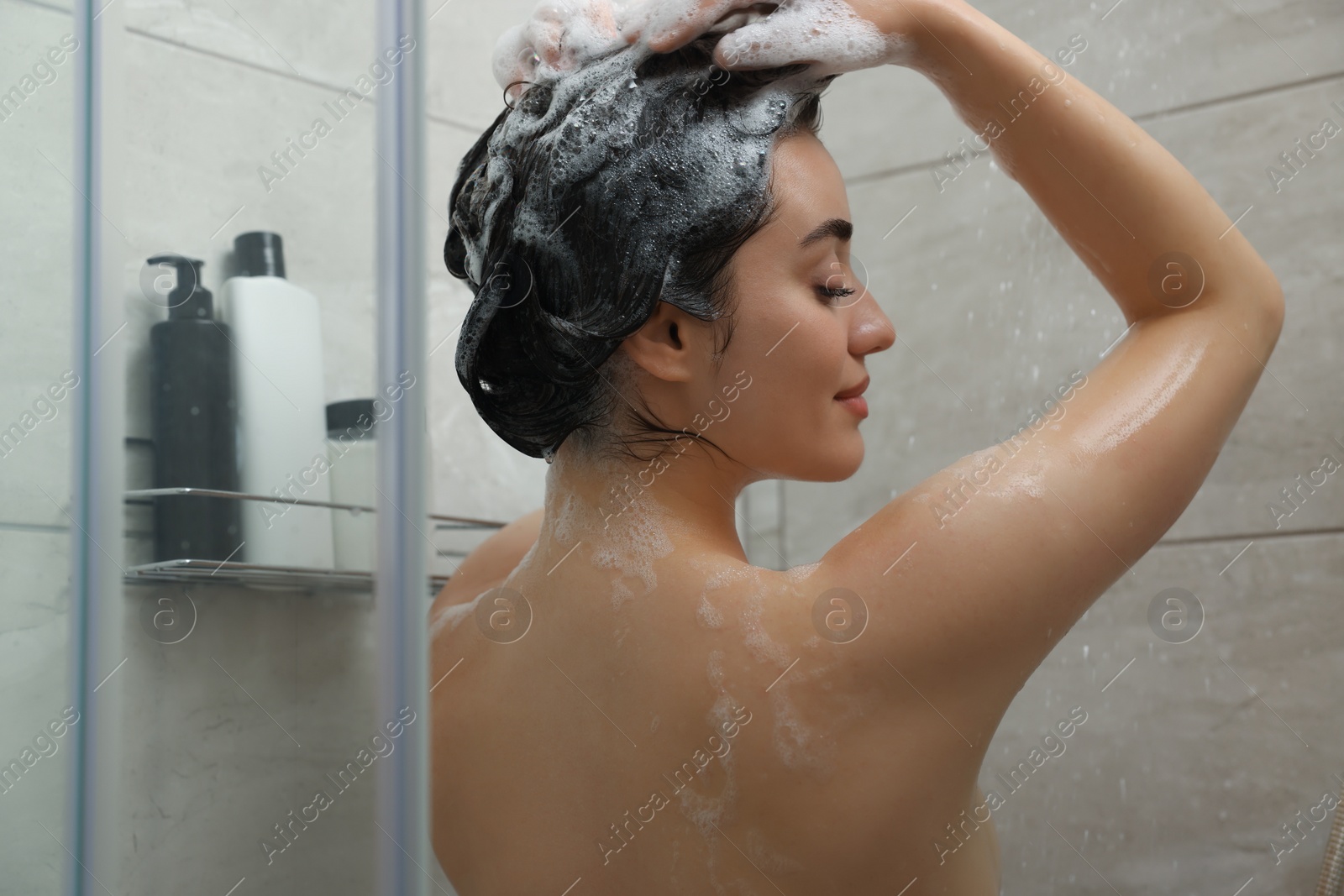 Photo of Beautiful woman washing hair with shampoo in shower, back view