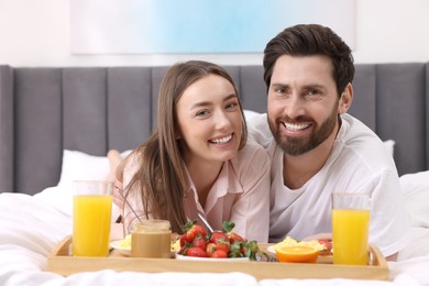 Photo of Family portrait of happy couple with tray of tasty breakfast on bed at home