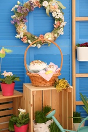 Photo of Basket with delicious Easter cakes, dyed eggs and flowers on wooden crate indoors