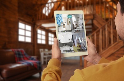 Man using smart home security system on tablet computer indoors, closeup. Device showing different rooms through cameras