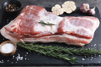 Photo of Piece of raw pork belly, rosemary, garlic and spices on table
