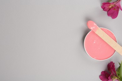 Photo of Wooden spatula, hot depilatory wax and flowers on light grey background, flat lay. Space for text