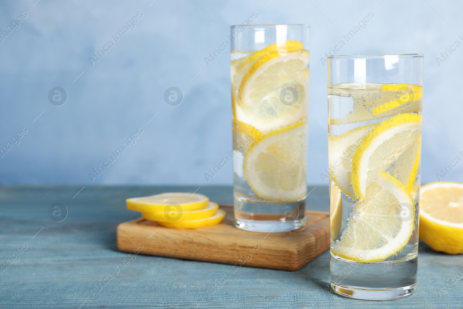 Photo of Soda water with lemon slices on blue wooden table. Space for text