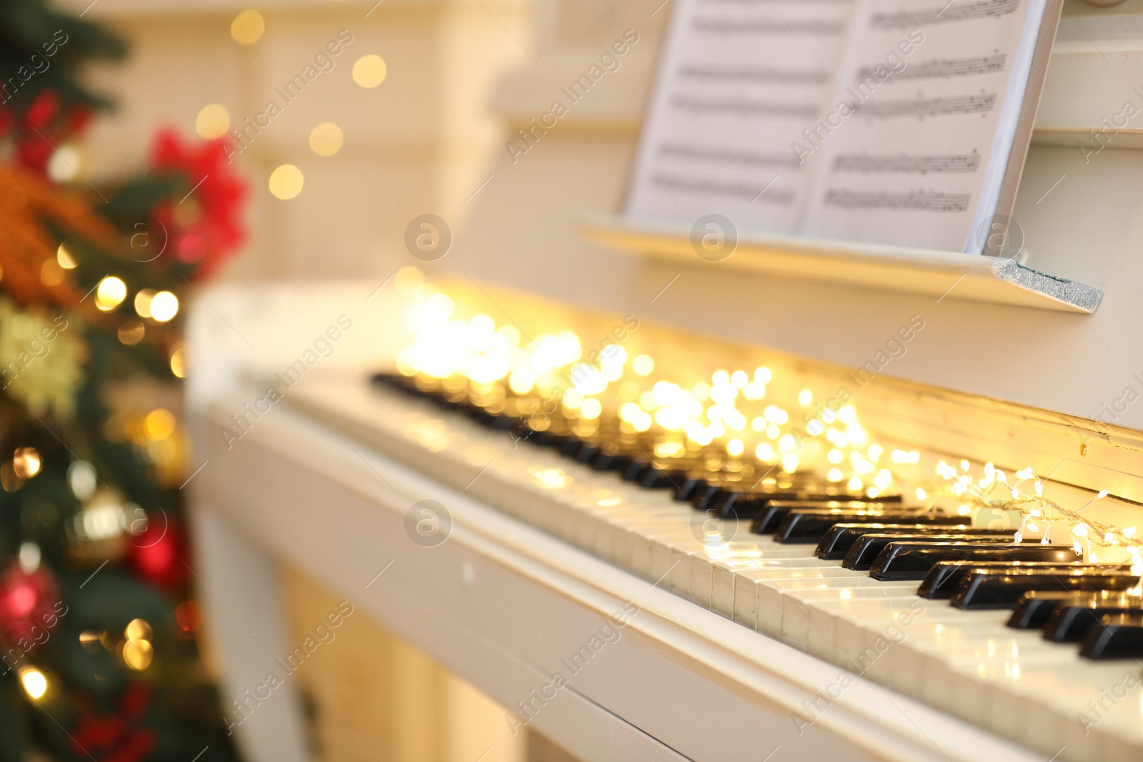 Photo of White piano with festive decor and note sheets indoors. Christmas music