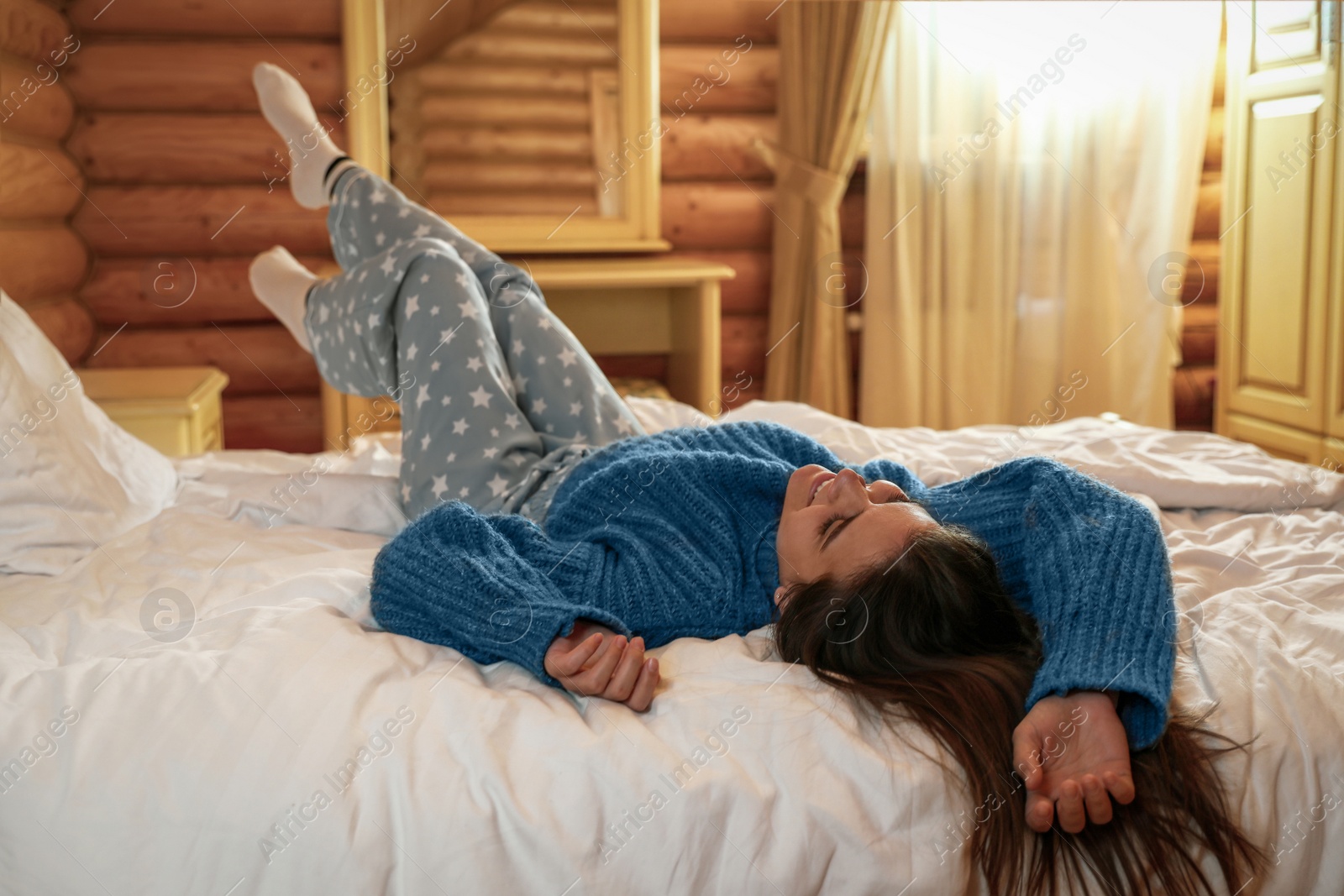 Photo of Young woman wearing warm sweater on bed at home