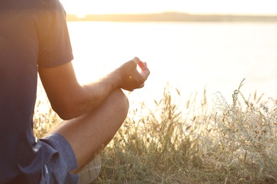 Man meditating near river on sunny day, closeup. Space for text