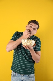 Man eating tasty popcorn on color background
