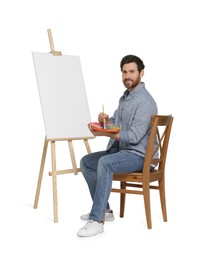 Photo of Happy man with brush and palette near easel with canvas. Creative hobby