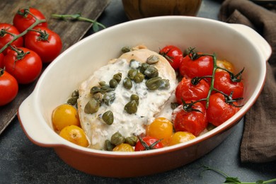 Photo of Delicious baked chicken fillet with capers, sauce and tomatoes in baking dish on grey table, closeup