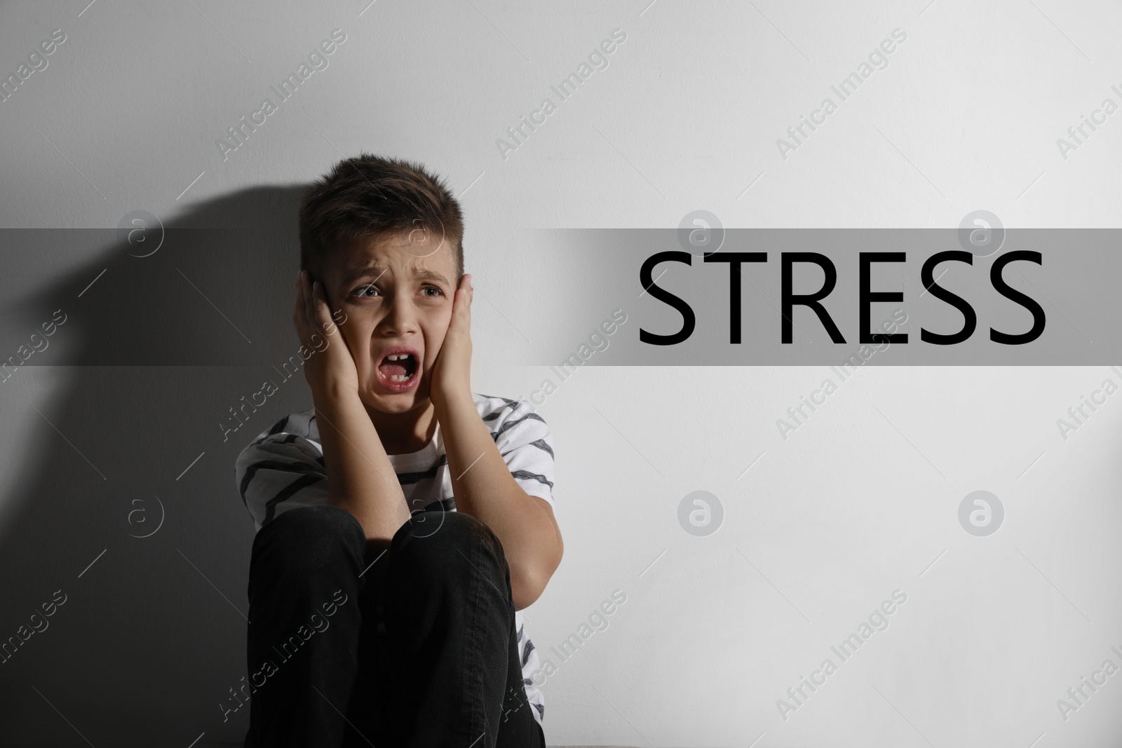 Image of Scared little boy near white wall and word STRESS 