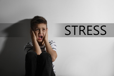 Scared little boy near white wall and word STRESS 