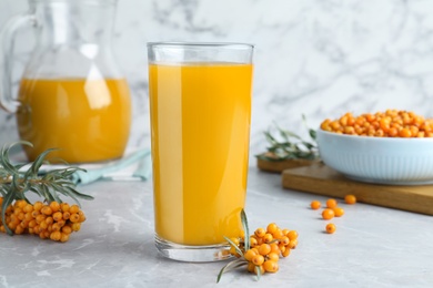 Photo of Sea buckthorn juice and fresh berries on white marble table, closeup