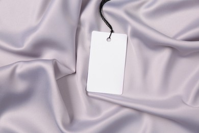 Photo of Blank tag on silver silky fabric, top view. Space for text
