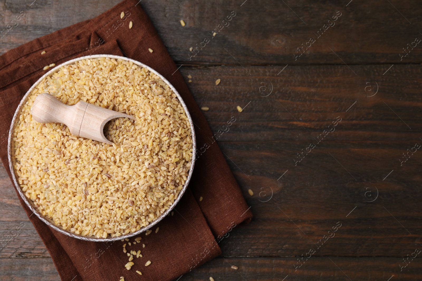 Photo of Bowl and scoop with raw bulgur on wooden table, top view. Space for text